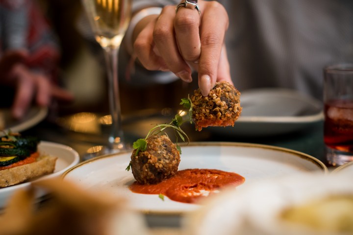 Hand dipping a crumbed food ball into red sauce on a plate.