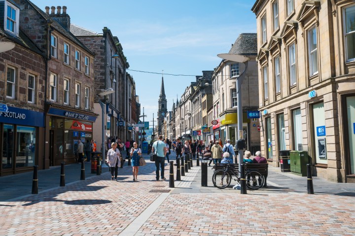People walking on a busy pedestrian street lined with shops and historic buildings.