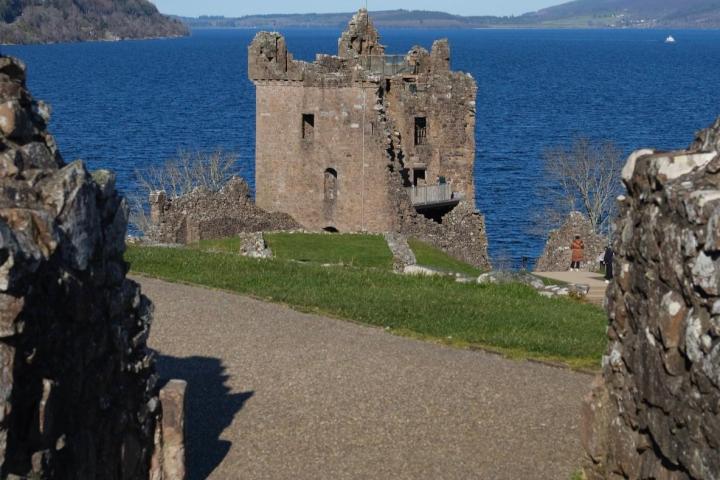 a stone castle next to a body of water with Urquhart Castle in the background