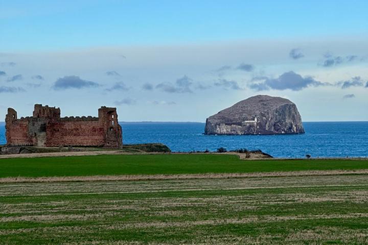 Ruined castle by the sea with a rocky island in the background under a blue sky.