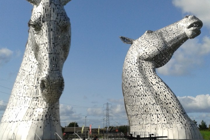 Two large metallic horse head sculptures under a blue sky.
