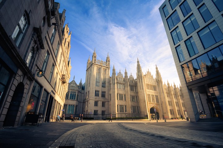 Gothic-style building with spires in a city square under a clear blue sky.
