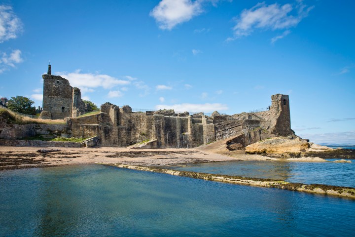 Ruined seaside castle with stone walls and tower under a clear blue sky.