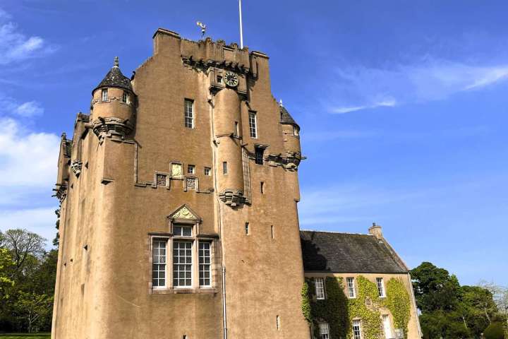 a castle with a clock tower in front of a brick building with Craigievar Castle in the background