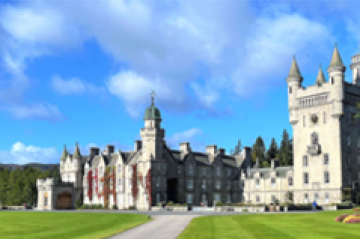 a castle with a clock tower with Balmoral Castle in the background