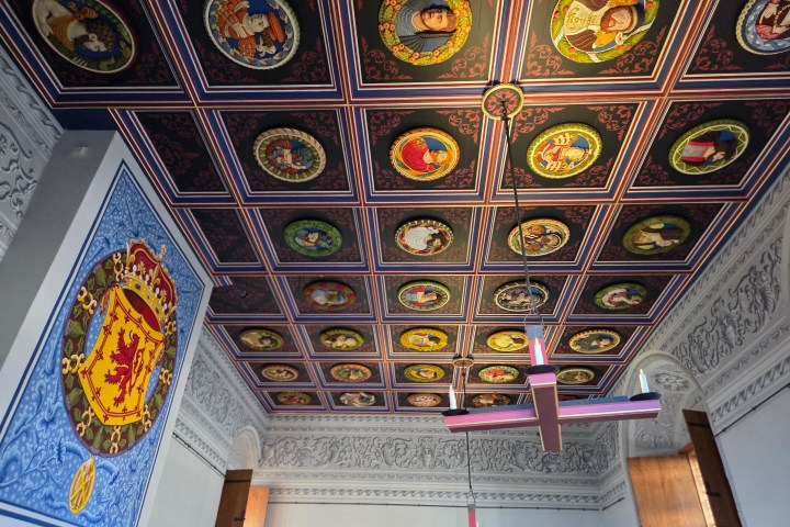 Ornate ceiling with painted portraits and a large heraldic shield on the wall.