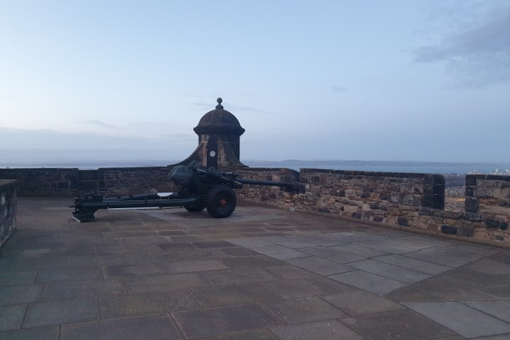 Cannon on a stone terrace with distant view of landscape and cloudy sky.