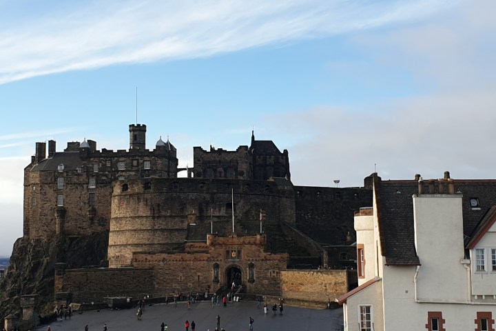Historical castle with tourists in the foreground under a partly cloudy sky.