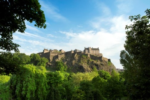 Castle on a hill surrounded by lush greenery under a blue sky.