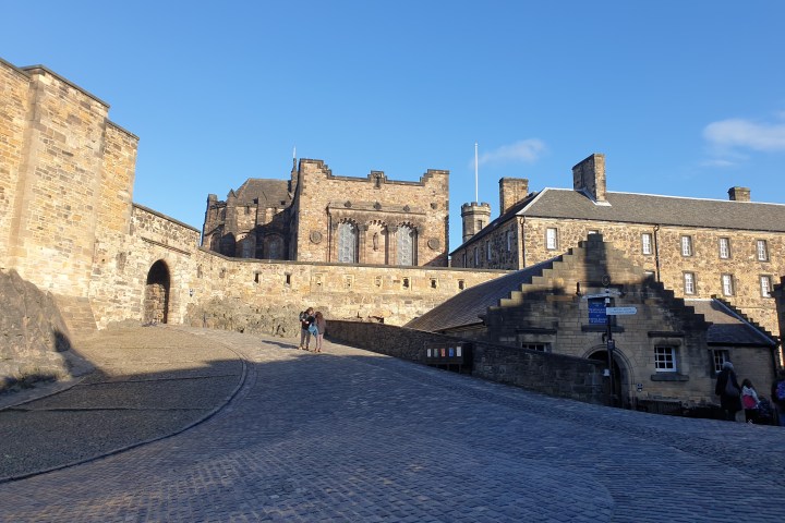 Stone castle with cobblestone pathway and sunlight, clear blue sky in background.