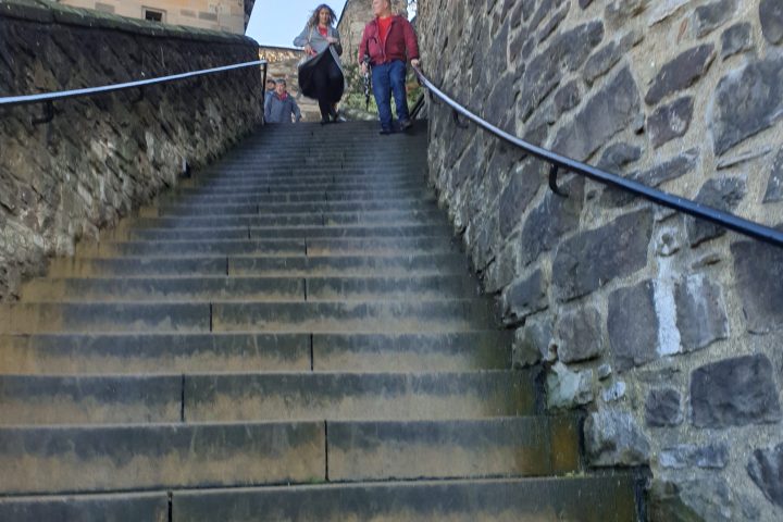 Stone stairs between castle walls with people descending.