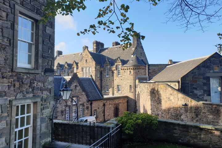 Historic stone buildings with sloped roofs and leafy branches under a blue sky.