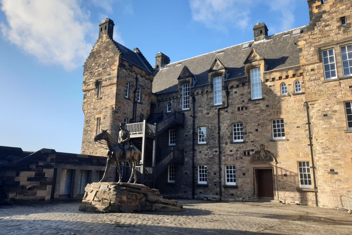 Stone building with staircases and a statue of a rider on horseback in a sunny courtyard.