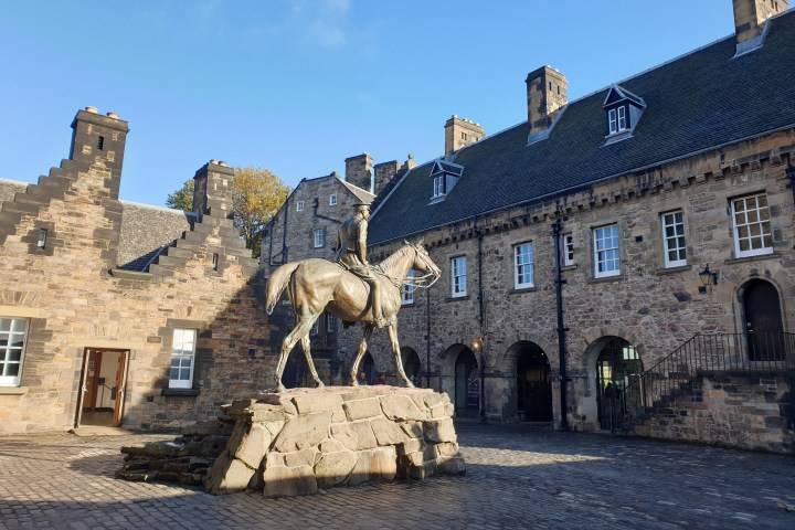 Statue of a soldier on horseback in a cobbled courtyard with historic stone buildings.
