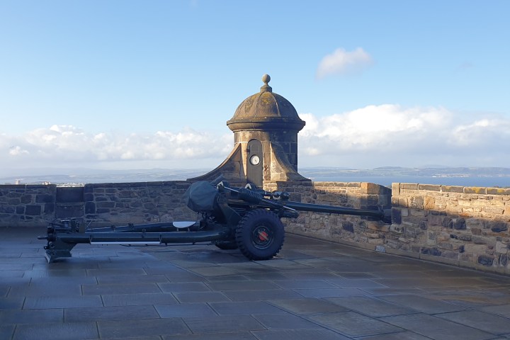 Cannon on castle wall with turret, blue sky and clouds in background.