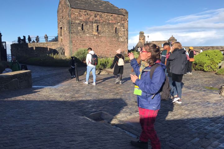 People walking near an old stone building with a clear blue sky.