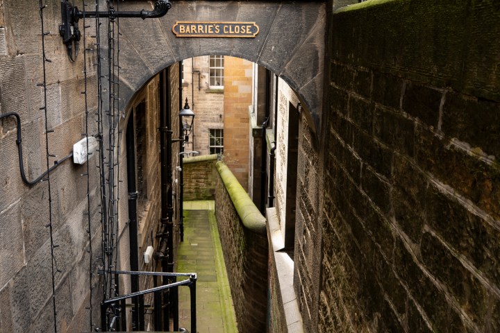 Narrow stone alleyway with steps, lamp, and archway sign 'BARRIE'S CLOSE'.
