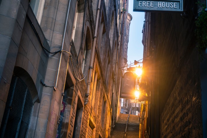 Narrow cobblestone alley with vintage pub sign and warm evening light.