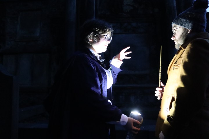 Two people at night, one holding a wand, both illuminated by a flashlight.