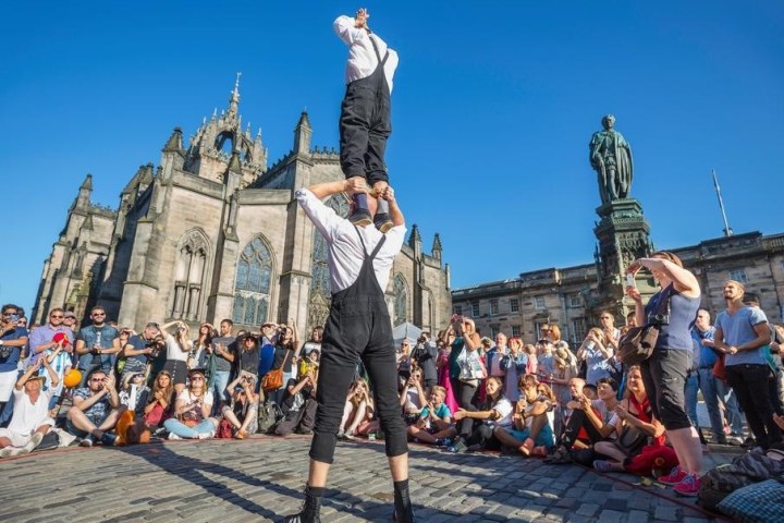 Performers in front of a crowd by historic buildings, blue sky.