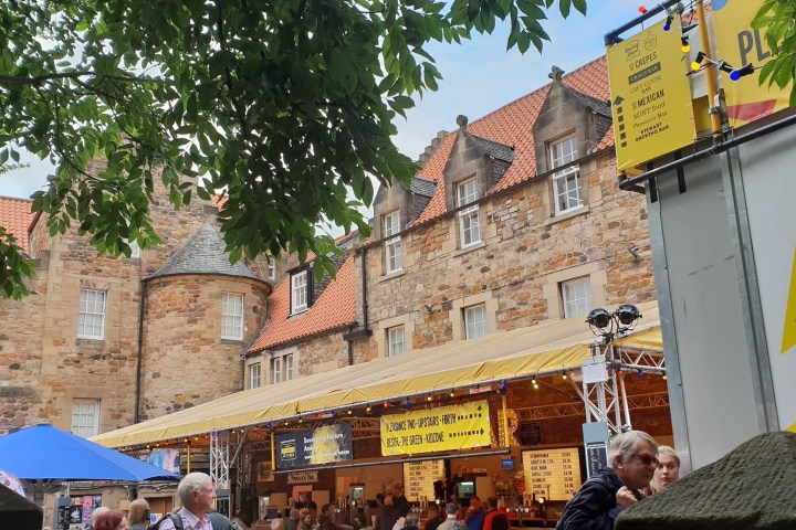 Outdoor event with crowd, booths, and historic buildings.