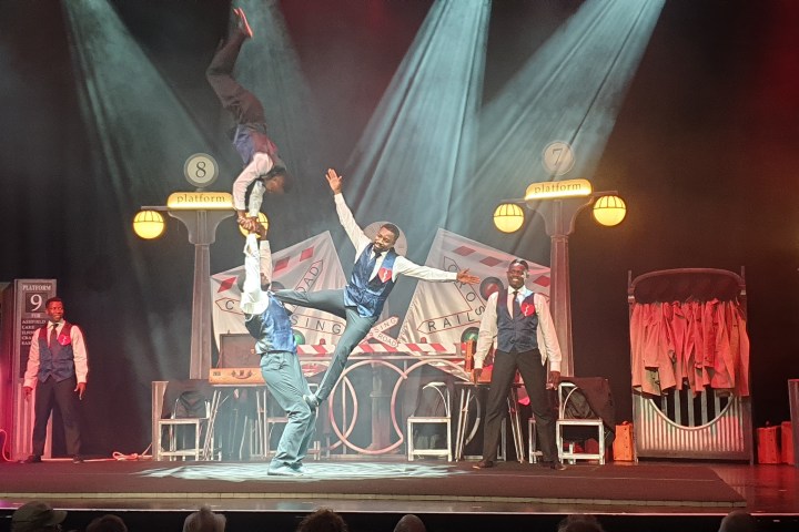 Performers in a theater act juggle and balance on stage with colorful lighting.
