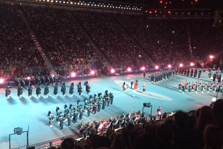 Large marching band performing in a stadium at night with audience watching.
