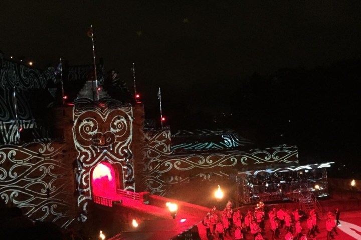 Nighttime outdoor performance with red lighting and projected patterns on a building.